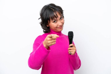 Genç Arjantinli şarkıcı kadın beyaz arka planda izole edilmiş mutlu bir ifadeyle ön tarafı işaret ediyor