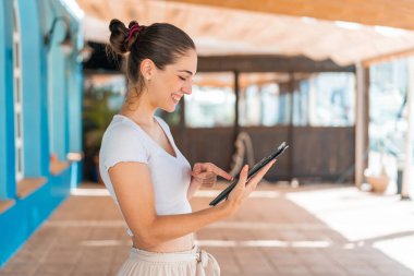 Açık havada güzel bir kadın tablet ekranına mutlu bir ifadeyle dokunuyor.