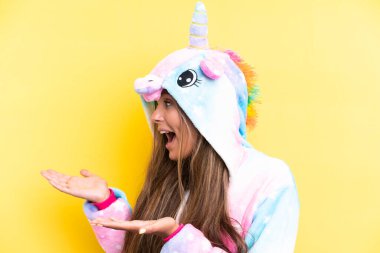 Tek boynuzlu bir pijama giyen beyaz bir kadın sarı arka planda, şaşırmış bir ifadeyle yan tarafa bakıyor.