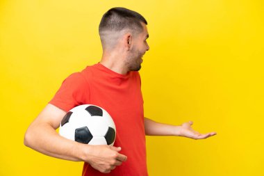 Futbol oynayan genç beyaz adam, sarı arka planda yalıtılmış, sürpriz bir ifadeyle yan yana bakarken...