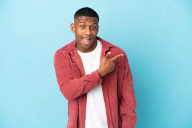 Mavi arka planda izole edilmiş genç latin adam şaşırmış ve işaret ediyor.