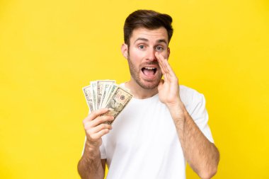 Kafkasyalı genç adam, sarı arka planda ağzı açık bağırarak bir sürü para alıyor.