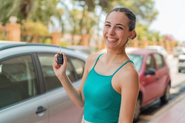 Dışarıda arabanın anahtarlarını tutan genç ve güzel bir kadın. Çok gülümsüyor.