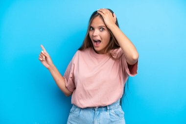 Mavi arka planda izole edilmiş genç beyaz kadın şaşırdı ve işaret etti.