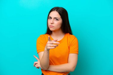 Mavi arka planda izole edilmiş genç beyaz kadın hayal kırıklığına uğramış ve ön tarafı işaret ediyor.