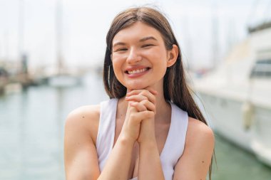 Genç, güzel bir kadın açık havada, mutlu bir ifadeyle.