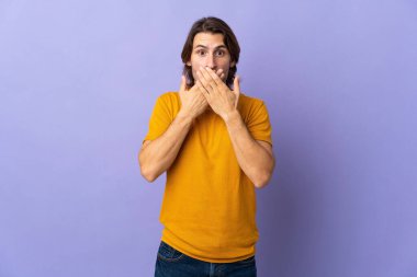 Mor arka planda izole edilmiş genç ve yakışıklı bir adam elleriyle ağzını kapatıyor.