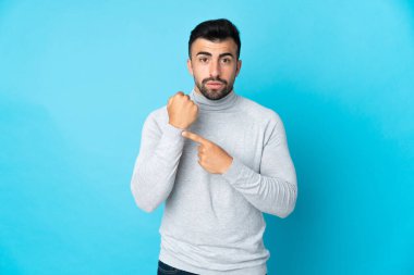 İzole edilmiş mavi arka planda beyaz bir adam geç kalma jesti yapıyor.