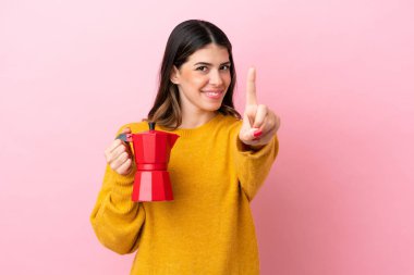 Pembe arka planda izole edilmiş kahve makinesini tutan genç İtalyan kadın parmağını kaldırıyor ve gösteriyor.