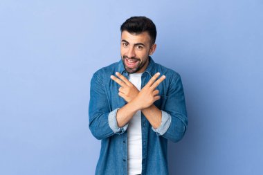 İzole edilmiş mavi arka plan üzerinde gülümseyen ve zafer işareti gösteren beyaz bir adam.