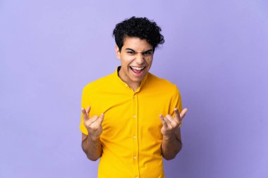 Genç Venezuelalı adam mor arka planda izole edilmiş boynuz hareketi yapıyor.