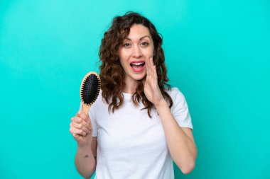 Mavi arka planda saç fırçası tutan beyaz bir kadın ağzı açık bağırıyor.