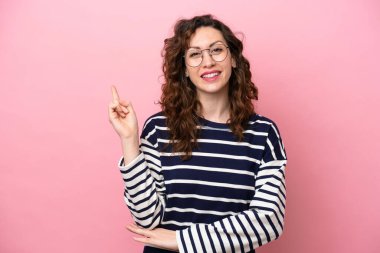 Pembe arka planda izole edilmiş genç beyaz kadın mutlu ve dik duruyor.