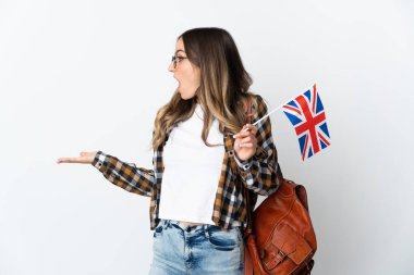 Beyaz arka planda, sürpriz bir ifadeyle izole edilmiş bir Birleşik Krallık bayrağını tutan genç Romen kadını