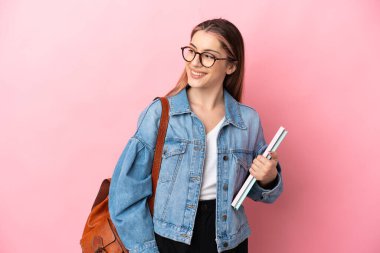 Pembe arka planda izole edilmiş genç beyaz bir kadın. Yan tarafa bakıyor ve gülümsüyor.