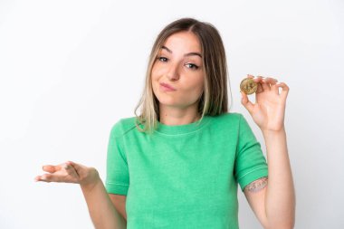 Beyaz arka planda izole edilmiş bir Bitcoin tutan genç Romen kadın, omuzlarını kaldırırken şüpheyle hareket ediyor