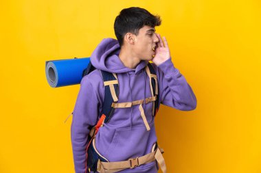 Sarı arka plan üzerinde büyük bir sırt çantası olan genç dağcı ağzı sonuna kadar açık bağırıyor.