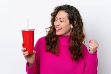 Young caucasian woman drinking soda isolated on white background celebrating a victory