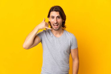 Sarı arka planda izole edilmiş genç yakışıklı bir adam telefon jesti yapıyor. Bana geri dönüş işareti ver.