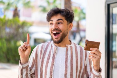 Açık havada cüzdan tutan yakışıklı bir Arap parmağını kaldırarak çözümü bulmayı umuyor.