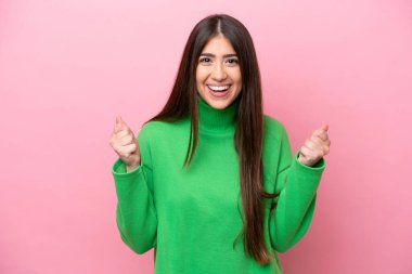 Pembe arka planda izole edilmiş genç beyaz kadın galibiyeti kutluyor.