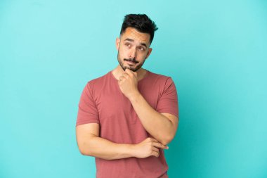 Kafkasyalı genç adam mavi arka planda izole edilmiş. Şüpheleri ve düşünceleri var.