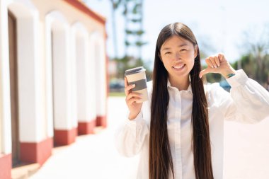 Güzel bir Çinli kadın açık havada kahvesini yudumlarken gururlu ve kendini beğenmiş.