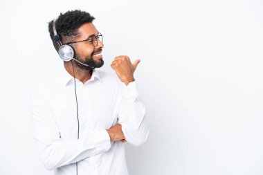 Tele pazarlamacı Brezilyalı beyaz arka planda izole edilmiş bir kulaklıkla çalışan bir adam bir ürün sunmak için kenarı işaret ediyor