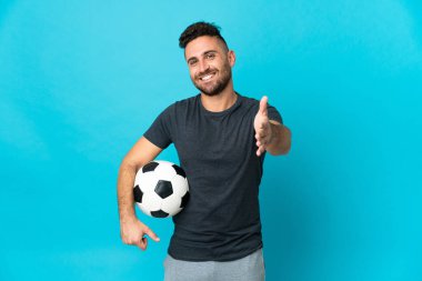 Futbolcu mavi arka planda izole edilmiş, iyi bir anlaşma için el sıkışıyor.