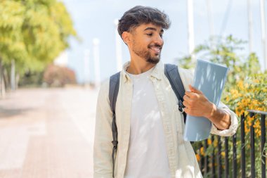 Genç bir Arap öğrenci açık havada neşeli bir ifadeyle.