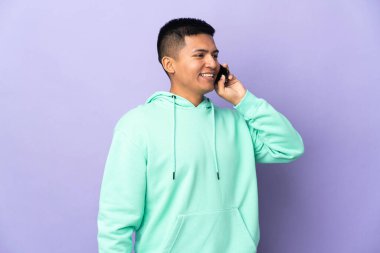 Genç Ekvadorlu adam mor arka planda izole edilmiş cep telefonuyla sohbet ediyor.