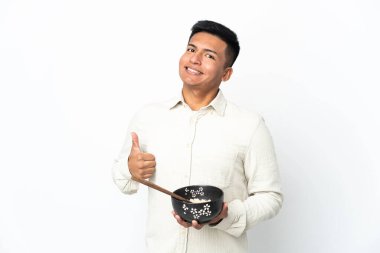 Ekvadorlu genç adam beyaz arka planda izole edildi. Başparmakları havada çünkü yemek çubuklarıyla bir kase erişte tutarken iyi bir şey oldu.