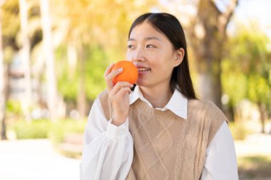 Dışarıdaki güzel Çinli kadın elinde mutlu bir ifadeyle bir portakal tutuyor.