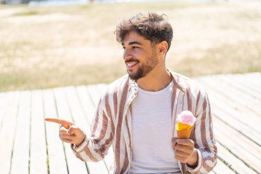 Açık havada kornet dondurması olan yakışıklı bir Arap, bir ürün sunmak için yan tarafı işaret ediyor.