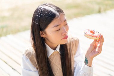 Dışarıdaki genç Çinli kadın elinde donut tutuyor.