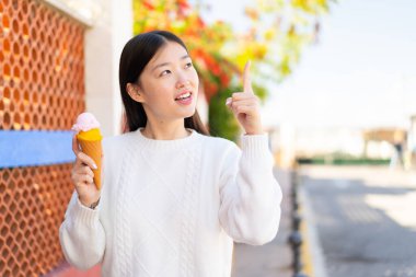 Açık havada kornet dondurması olan güzel Çinli kadın çözümün farkına varmak için parmağını kaldırıyor.