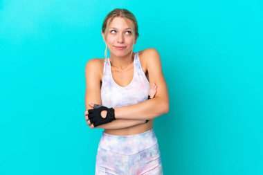 Beyaz kadın, mavi arka planda izole edilmiş. Omuzlarını kaldırırken şüpheyle hareket ediyor.