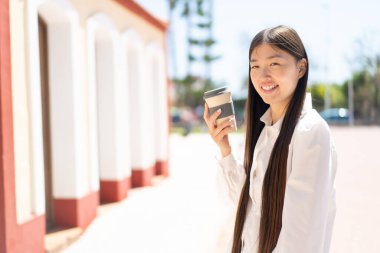 Güzel bir Çinli kadın açık havada kahveyi alıp götürüyor ve gülümsüyor.