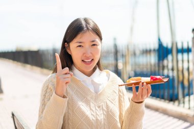 Genç Çinli kadın elinde sashimi tutarak harika bir fikri işaret ediyor.