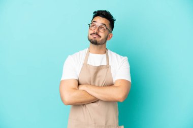 Restoran garsonu beyaz adam mavi arka planda izole edilmiş gülümserken yukarı bakıyor.
