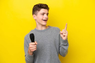 Singer Teenager sarı arka planda izole edilmiş bir mikrofonu eline aldı. Çözümü bulmak için parmağını kaldırdı.