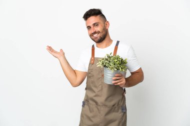 Bahçıvan, beyaz arka planda bir bitki tutuyor. Gelmesi için ellerini yana uzatıyor.