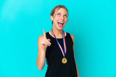 Mavi arka planda izole edilmiş madalyaları olan genç beyaz kadın yukarı bakıyor ve şaşırıyor.