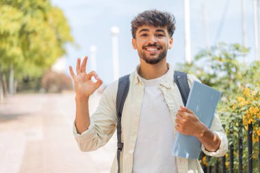 Açık havada gezen genç Arap öğrenci parmaklarıyla işaret veriyor.