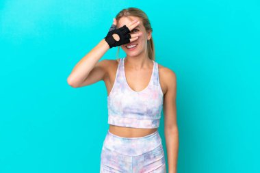 Mavi arka planda izole edilmiş beyaz bir kadın. Gözleri elleriyle kaplıyor ve gülümsüyor.