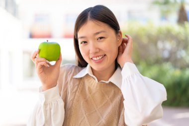 Dışarıdaki güzel Çinli kadın elinde mutlu bir ifadeyle bir elma tutuyor.