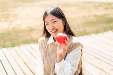 Açık havada elmalı genç bir Çinli kadın çok fazla gülümsüyor.