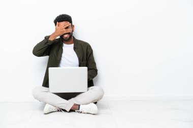 Dizüstü bilgisayarı olan genç Brezilyalı bir adam yerde oturuyor. Beyaz tenli, gözleri kapalı ve gülümsüyor.