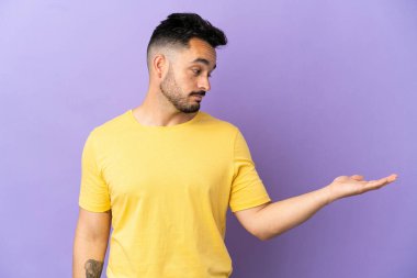 Mor arka planda izole edilmiş genç beyaz adam, kopyalama alanını şüphe ile tutuyor.