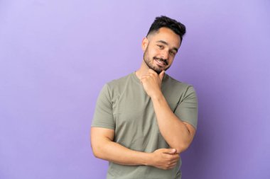 Mor arka planda izole edilmiş genç beyaz adam mutlu ve gülümsüyor.